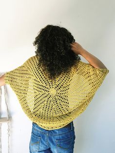 a woman standing in front of a white wall wearing a yellow crochet shawl