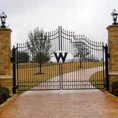 an iron gate with the letter w on it is in front of a brick driveway