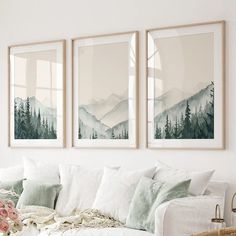 three framed pictures hang on the wall above a white couch in a living room with pillows and blankets