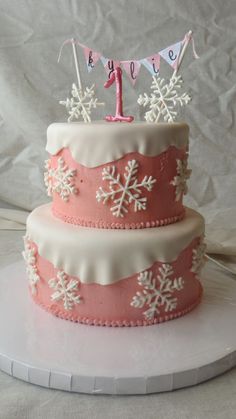 a pink and white cake with snowflakes on it's sides, topped with a number one