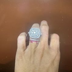 a woman's hand with a diamond ring on top of her finger, in front of a brown background