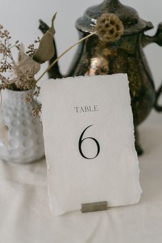 a table number is placed next to a teapot and vase with flowers in it