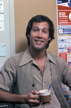 a man holding a coffee cup in his right hand and standing next to a wall with advertisements on it