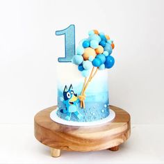 a birthday cake with blue and orange balloons on it, sitting on a wooden stand