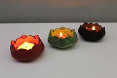 three different colored candles sitting on top of a white table next to eachother