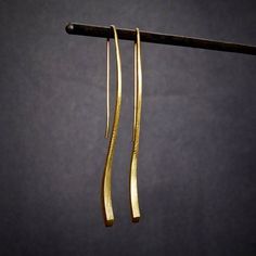 two long gold - plated earrings hanging from a hook on a black background,