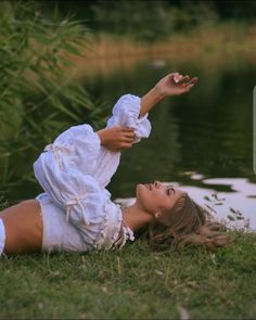 a woman laying on the ground next to a body of water with her arms outstretched