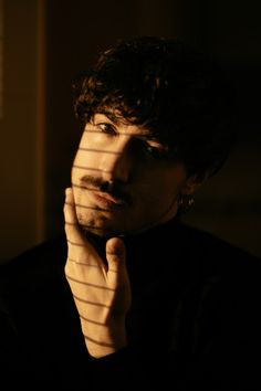 a man with his hand on his chin looking at the camera while standing in front of a window