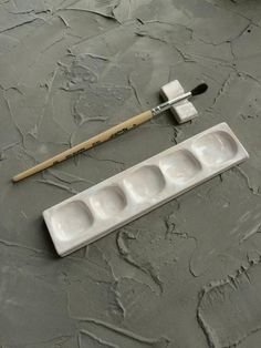 a paintbrush and two empty trays sitting on a gray surface next to a brush