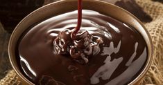 chocolate ganache sauce being poured into a bowl with nuts on the side and then drizzled over it