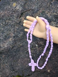 a doll's hand with a purple bracelet and cross charm on top of it