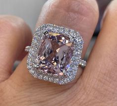 a person's hand holding an engagement ring with a pink diamond in the center