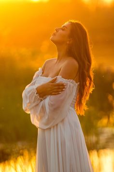 a woman in a white dress is looking up into the sky with her arms crossed