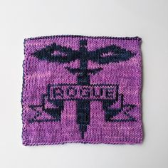 a purple and black knitted square with a cross on the front that says,