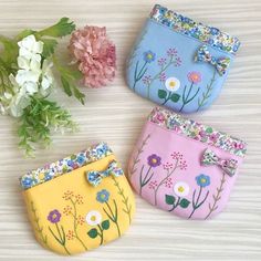 three small purses with flowers on them sitting next to some pink and white flowers