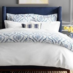 a bed with blue and white comforter in a bedroom next to a painting on the wall