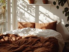 an unmade bed in front of a window with potted plants