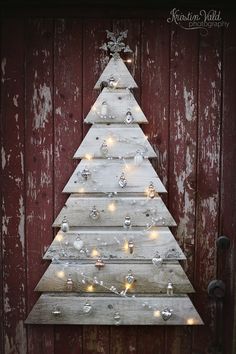 a wooden christmas tree with lights hanging from it's sides in front of a barn door