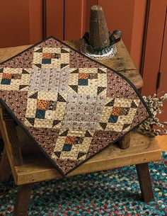 a quilted table topper sitting on a wooden bench in front of a red door