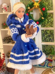 a doll holding a teddy bear in front of a christmas wreath