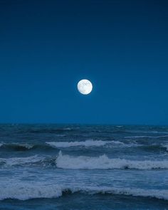 the moon is setting over the ocean with waves in the foreground and dark blue sky