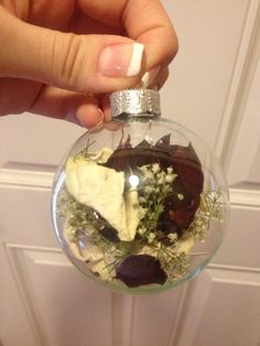 a hand holding a glass ornament filled with flowers and leaves in front of a door