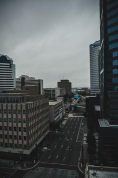 an empty city street with tall buildings in the background and dark clouds overhead, on a gloomy day