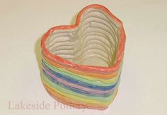 a rainbow heart shaped bowl on a white table with the lid open and stacked in it