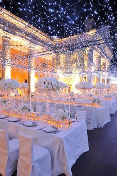 a banquet hall with tables and chairs covered in white linens, lit up by fairy lights