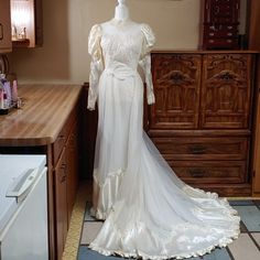 a white wedding dress on display in a kitchen next to a dresser and cabinets with drawers