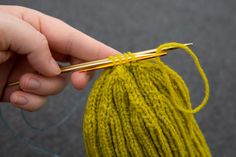 a hand holding a knitting needle over a ball of yarn