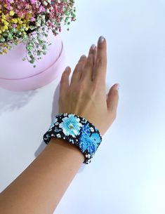 a woman's hand with a beaded bracelet on her wrist next to a flower pot