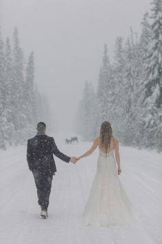 a bride and groom walking in the snow holding hands