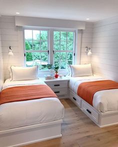 two beds in a room with white walls and wood flooring, one has an orange blanket on it