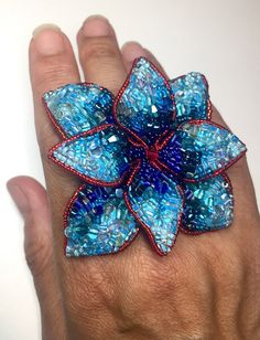 a person's hand holding a blue and red flower brooch