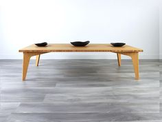 two black bowls sit on top of a wooden table in front of a white wall