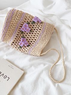 a straw bag with flowers on it and a book laying next to it, sitting on a bed