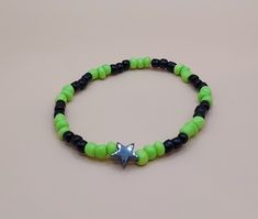 Green and black seed beads featuring a black star on an elastic bracelet. Trendy Black Beaded Bracelets With Tiny Beads, Casual Beaded Bracelets With Star Charm For Gift, Black Bracelets With Star Charm As Gift, Casual Adjustable Beaded Bracelet With Star Charm, Handmade Adjustable Star-shaped Stretch Bracelet, Handmade Adjustable Star Stretch Bracelet, Handmade Adjustable Star Shaped Stretch Bracelet, Handmade Star-shaped Casual Bracelets, Adjustable Black Bracelet With Star Charm