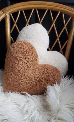 two heart shaped pillows sitting on top of a white fur covered chair next to a black wall