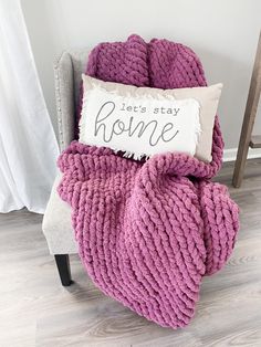 a purple blanket sitting on top of a white chair next to a pillow that says let's stay home