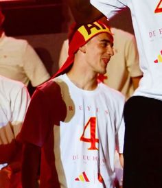 a man wearing a red and yellow hat standing next to other men in white shirts