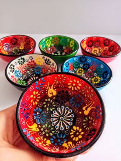 a hand is holding a colorful bowl with different designs on it and five other bowls in the background