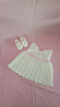 Adorable hand crochet white dress with shoes to complete the outfit.  It can be used for a formal occasion or just for a day out shopping with the girls. Made from a soft, light weight 100% Acrylic yarn. Size is 3-6 months. Set includes: Dress featuring rippled shell stitch pattern, one button closure on back, a cute ribbon with pink hearts at the waist that ties in the back and  a cute stitch on the edges for a finished look. Dress measures 9 inches across at chest and 13 inches long from shoulder to bottom edge. Shoes feature a strap with button closure on the side for a secure fit. Shoe measures 4 inches long x 2.25 inches wide x 1.5 inches tall.  **Please be aware measurements are approximations due to possible slight stretching while measuring. **Size may be smaller or larger on your Cute Hand Knitted White Dresses, Cute White Crochet Lace Dress, Cute Hand-knitted White Dress, White Crochet Lace Dress Cute Style, Cute White Hand Knitted Dress, Cute White Hand-knitted Dress, Cute Cream Baptism Dress For Summer, White Lace Baptism Dress For Summer, Handmade Crochet Dress For Summer