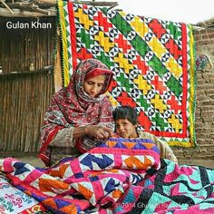 a woman sitting next to a child on top of a bed covered in quilts