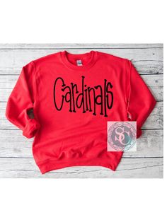 These Cardinals handwritten shirts are a perfect addition to your school spirit wear and are super cozy!  ❗️Sizes: Toddler-2T-5T  Youth XS-XL  Adult S-XL  Adult 2X Adult 3X Available in short sleeve, long sleeve and sweatshirts!  Shirts are all unisex sizing!  The shirt has cardinals printed and pressed onto the shirt! Cardinals is written in black!  If you would like to request a custom order, please send us a message!! Cardinals School Spirit Shirts, Cardinals Spirit Wear, Cardinal School Spirit Shirts, Casual T-shirt For School Football Season, Red Sweatshirt For School In Fall, School Spirit Graphic Sweatshirt For Baseball Season, Red Team Spirit Sweatshirt For Game Day, School Spirit Graphic Print Sweatshirt For Baseball Season, Red Game Day Sweatshirt Fan Apparel