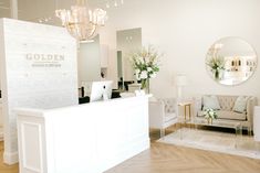 a reception area with white furniture and chandelier hanging from the ceiling in front of a mirror