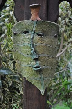 a green mask hanging from the side of a wooden pole in front of some bushes