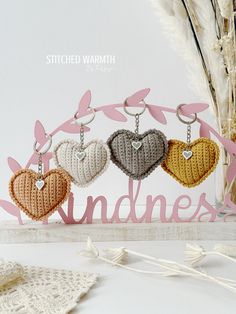 three crocheted heart keychains are hanging from a sign that says kindness