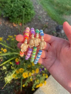 a person is holding several colorful bracelets in their hand and there are flowers behind them