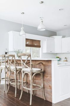 a kitchen with white cabinets and wooden floors, two bar stools in the center